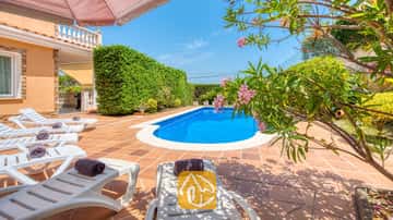 Piscine extérieure privée à la Villa Primavera, entourée d'une terrasse carrelée, de chaises longues blanches agrémentées de serviettes sombres enroulées et de branches de lauriers roses en fleurs.