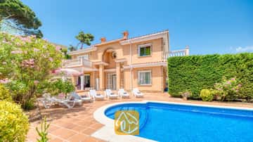 Piscine privée et terrasse à la Villa Primavera, dotées de transats blancs, de sols en terre cuite et d'une façade couleur pêche sur deux étages sous un ciel bleu.