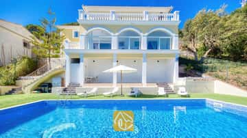 Extérieur de la Villa Sunrise présentant une piscine rectangulaire carrelée de bleu, des transats blancs et une villa jaune à plusieurs étages dotée de portes vitrées en arc sous un ciel dégagé.