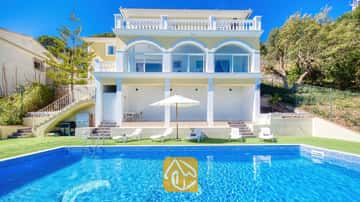 Extérieur de la Villa Sunrise présentant une piscine rectangulaire carrelée de bleu, des transats blancs et une villa jaune à plusieurs étages dotée de portes vitrées en arc sous un ciel dégagé.