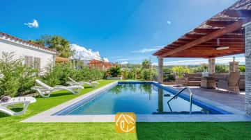 Piscine extérieure et terrasse couverte à la Villa Palmera, comprenant des transats blancs en plastique sur gazon synthétique et une pergola en bois avec des assises en osier.