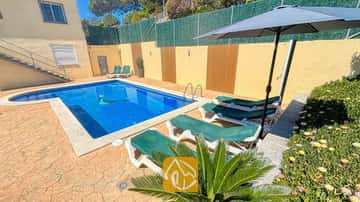 Piscine extérieure privée à la Villa Holiday, entourée de transats verts, d'un parasol sombre et d'un sol de patio en pierre.