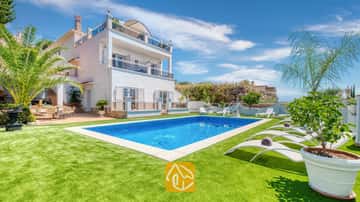 Piscine privée et chaises longues blanches sur une pelouse verdoyante à la Villa Maribel en Espagne, mettant en valeur une villa blanche à étages avec balcons et palmiers.