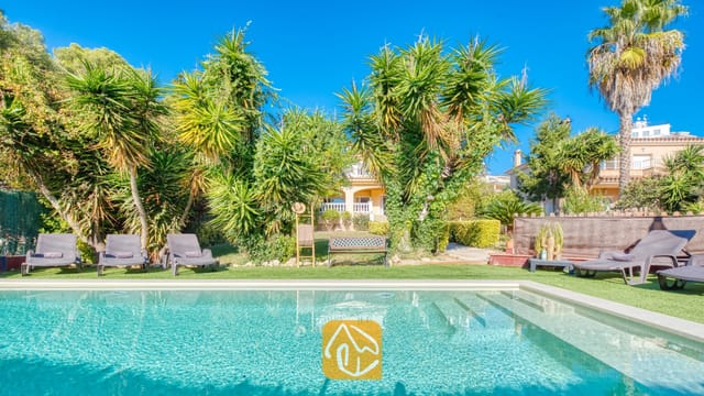 Piscine extérieure avec marches intégrées à la Villa Summertime, entourée de gazon synthétique, de plusieurs chaises longues et de palmiers tropicaux sous un ciel bleu.