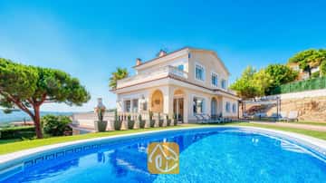 Piscine privée au premier plan avec la Villa Ibiza, une maison couleur crème à deux étages, une pelouse verte et des cactus en pot sous un ciel bleu éclatant.