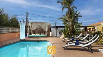 Piscine privée avec toboggan bleu, terrasse en bois, transats gris accompagnés de serviettes bleues, et cabana drapée à la Villa Soleia.