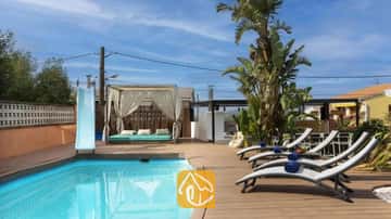 Piscine privée avec toboggan bleu, terrasse en bois, transats gris accompagnés de serviettes bleues, et cabana drapée à la Villa Soleia.