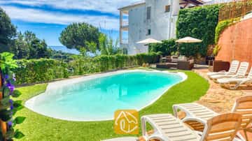 Piscine privée avec chaises longues et salon de jardin à la Villa Sunny Beach en Espagne, comprenant une pelouse verdoyante, des parasols blancs et une vue sur la mer en arrière-plan.