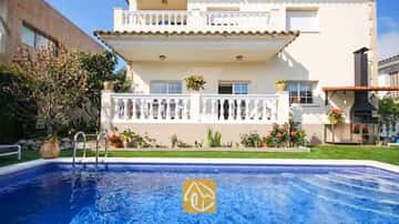 Piscine privée aux eaux carrelées de bleu devant la façade extérieure de la Villa Mercedes Fenals, dotée de balcons à balustrades blanches, d'une pelouse verdoyante et d'un barbecue en briques extérieur.