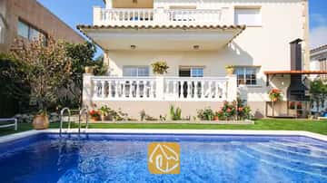 Piscine privée aux eaux carrelées de bleu devant la façade extérieure de la Villa Mercedes Fenals, dotée de balcons à balustrades blanches, d'une pelouse verdoyante et d'un barbecue en briques extérieur.